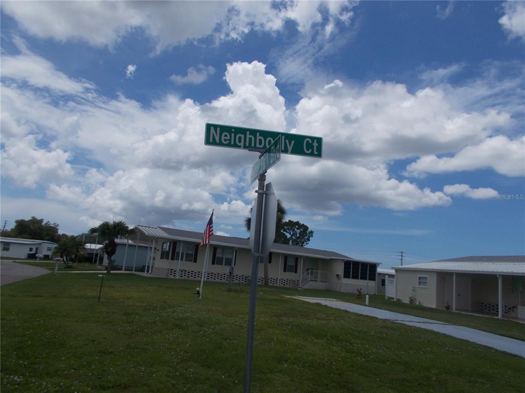 A street sign stands in front of a residential neighborhood with houses and a flag — 6786 NEIGHBORLY COURT, NORTH PORT, FL