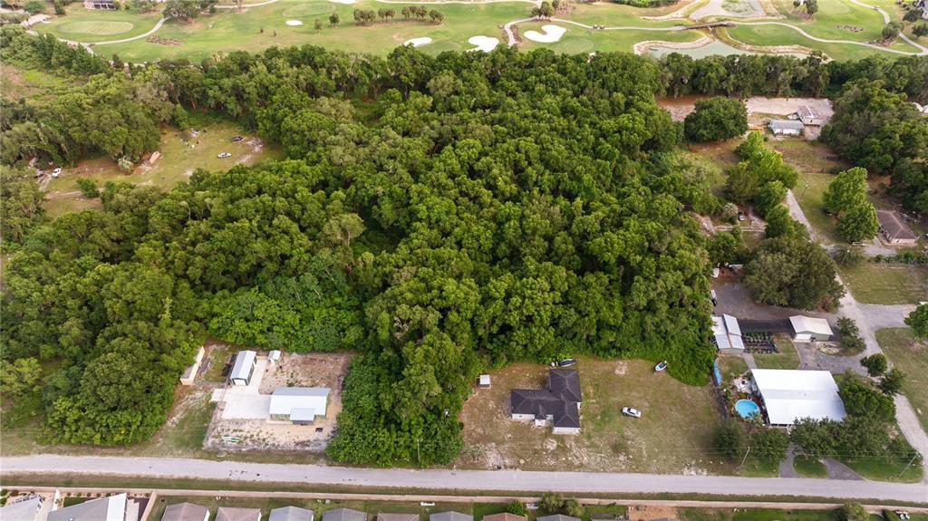 An aerial view shows a large wooded lot situated between several houses and a golf course — 0 SR 144, WILDWOOD, FL