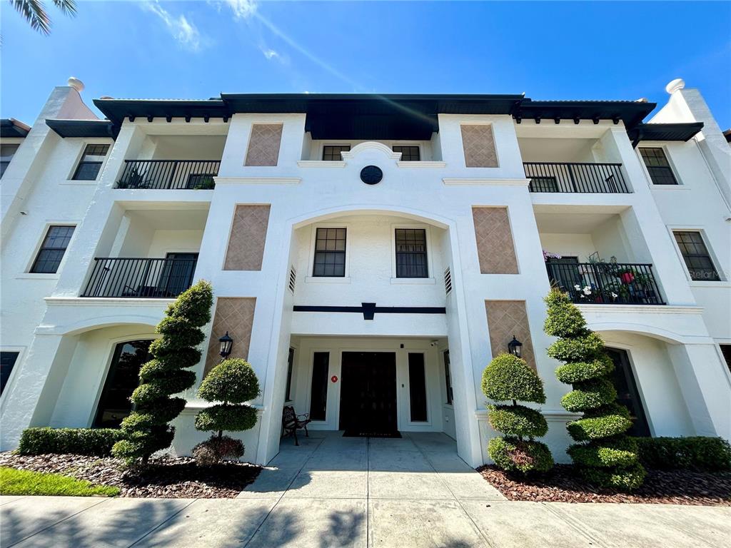 A three-story white apartment building with balconies and manicured spiral topiary trees at the entrance — 5550 E MICHIGAN STREET UNIT 2208, ORLANDO, FL