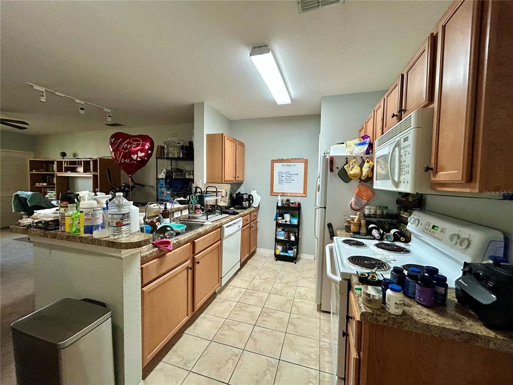 A kitchen features light wood cabinets, laminate countertops, tile flooring, and white appliances — 5550 E MICHIGAN STREET UNIT 2208, ORLANDO, FL