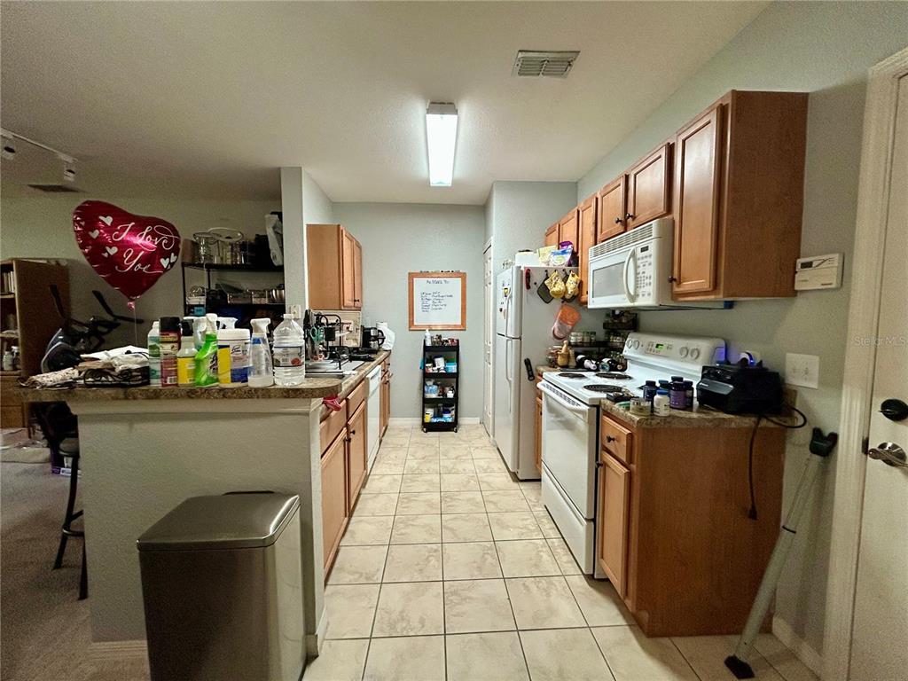 A kitchen features light wood cabinets, tile flooring, white appliances, and a breakfast bar — 5550 E MICHIGAN STREET UNIT 2208, ORLANDO, FL