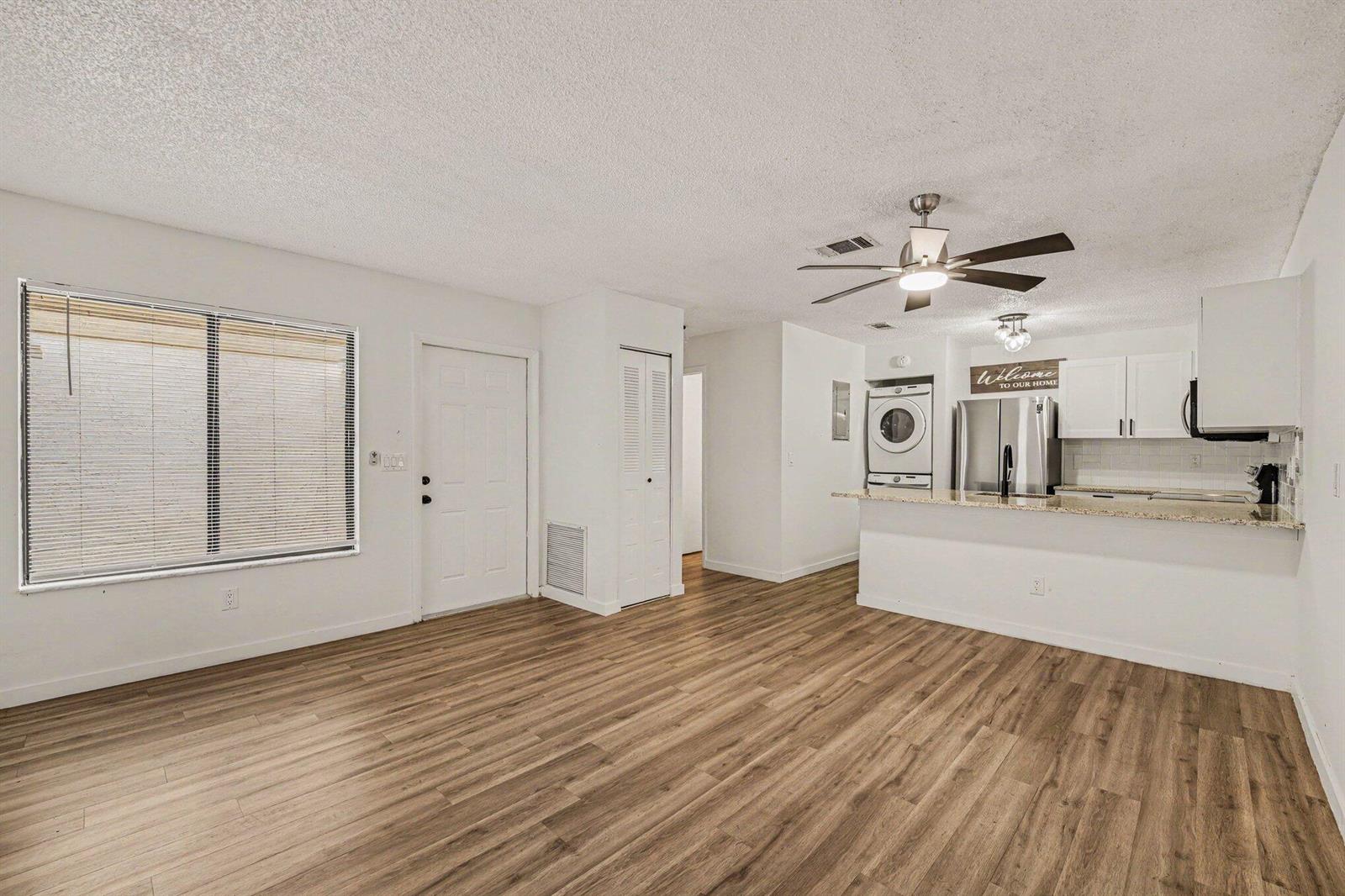 An open-concept living area with wood-look flooring, a ceiling fan, and an adjacent kitchen — 1011 NE Abada Ct Court NE # 110, Palm Bay FL 32905, PALM BAY, FL