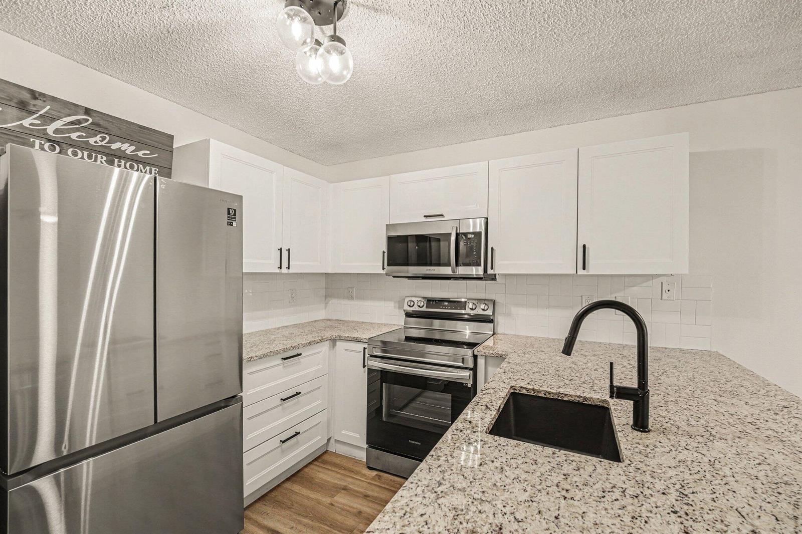 A kitchen features white cabinets, granite countertops, stainless steel appliances, and a black faucet — 1011 NE Abada Ct Court NE # 110, Palm Bay FL 32905, PALM BAY, FL