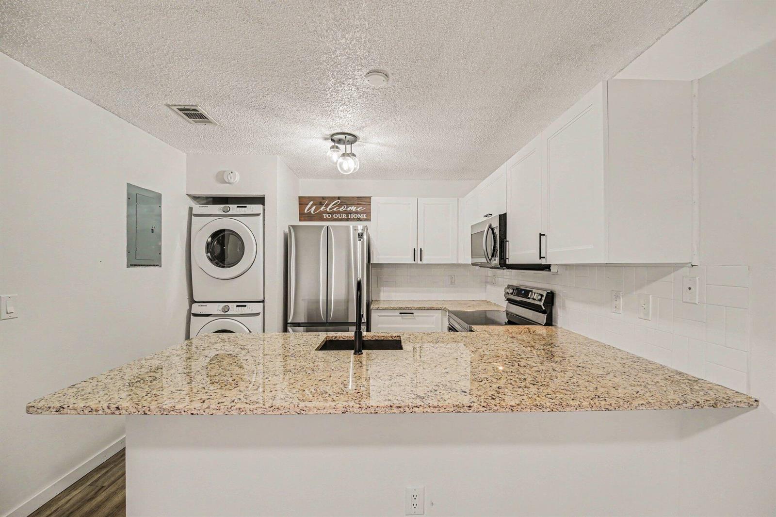 A kitchen features white cabinets, granite countertops, stainless steel appliances, and a stacked laundry unit — 1011 NE Abada Ct Court NE # 110, Palm Bay FL 32905, PALM BAY, FL