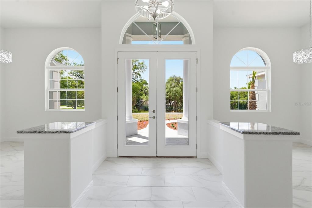 A bright entryway features white walls, marble-look tile floors, dual granite-topped pedestals, and glass-paneled doors — 421 W CHASE STREET, HERNANDO, FL