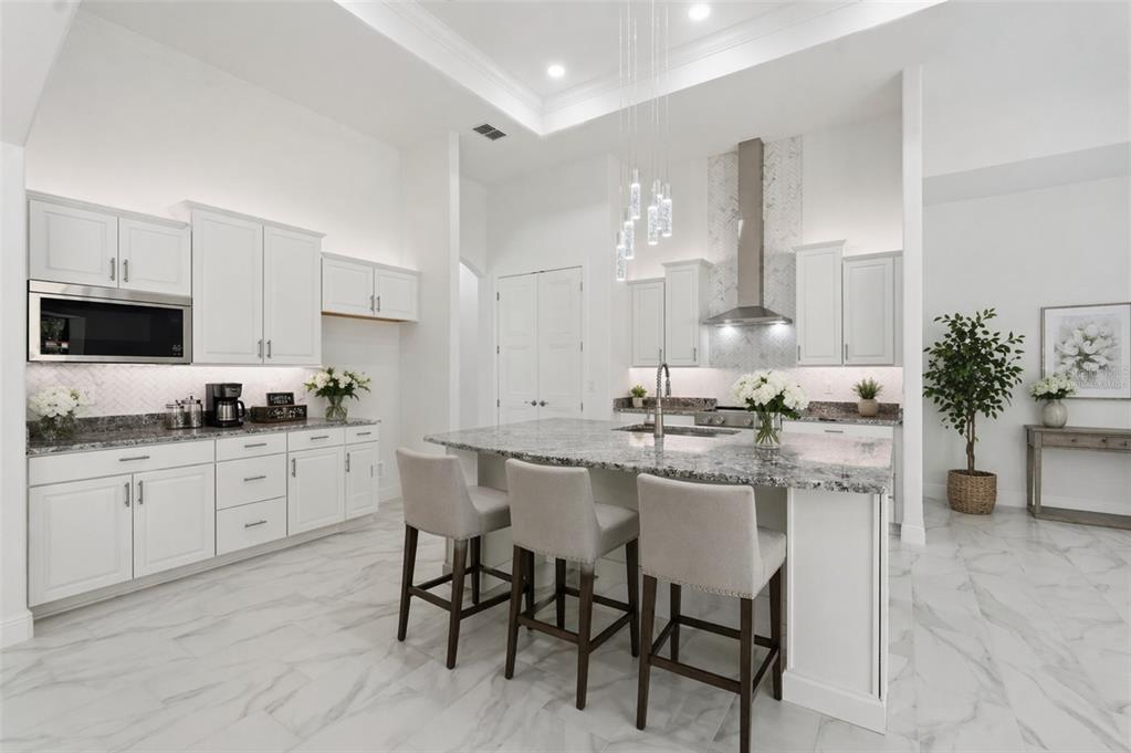 A bright kitchen features white cabinetry, a granite island with three stools, and marble flooring — 421 W CHASE STREET, HERNANDO, FL