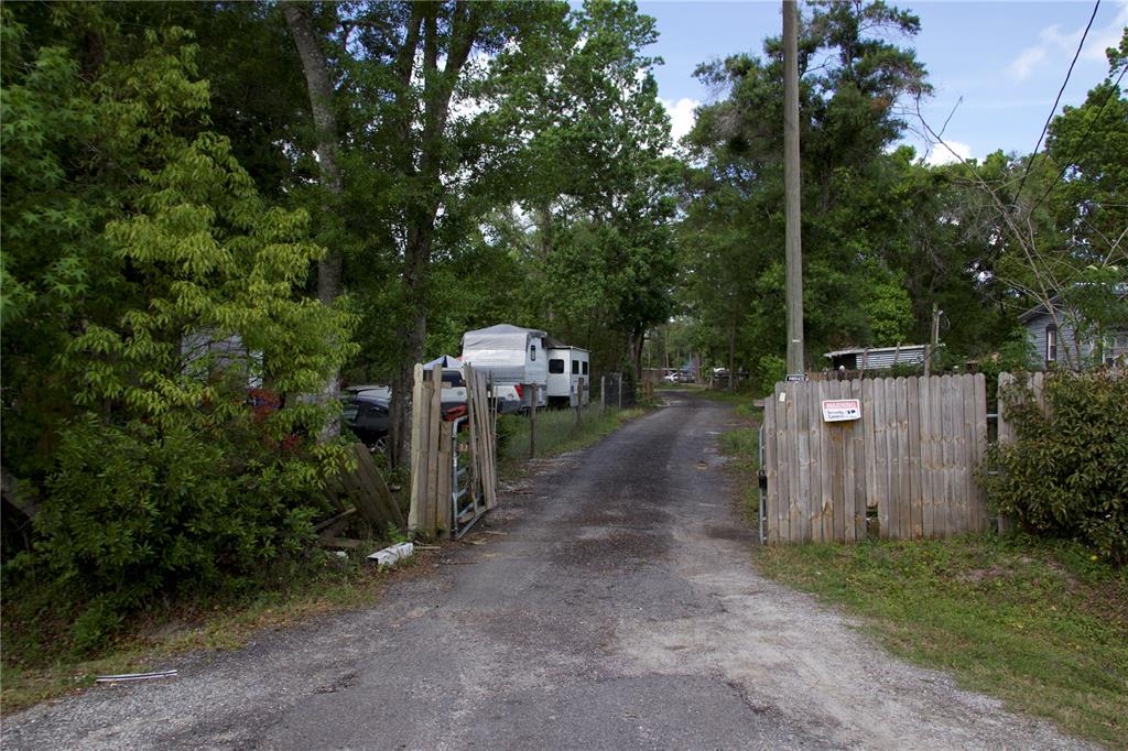 A gravel driveway leads through a wooden gate toward a parked camper in a wooded area — 1920 10TH STREET, ORLANDO, FL