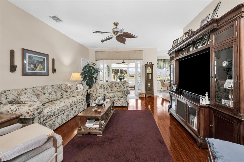 A living room features floral sofas, a dark wood entertainment center, and hardwood floors — 24615 BUCKINGHAM WAY, PUNTA GORDA, FL