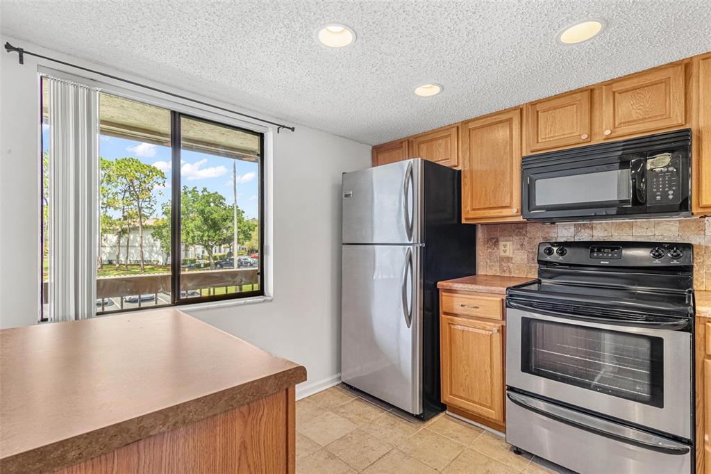 A kitchen features wood cabinets, stainless steel appliances, tile flooring, and a window with views — 108 WOODLANDS COURT UNIT 108, OLDSMAR, FL