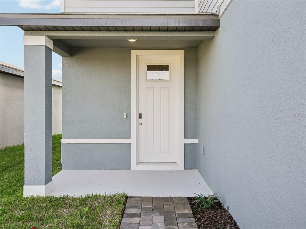 A gray exterior wall with a white front door and a covered concrete porch — 11336 BELLEWOOD TERRACE, PARRISH, FL