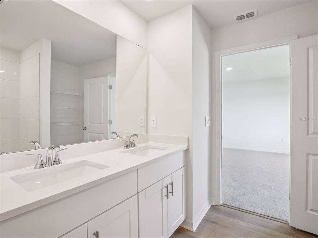A modern bathroom features a white double vanity with a large mirror and adjacent bedroom — 11336 BELLEWOOD TERRACE, PARRISH, FL