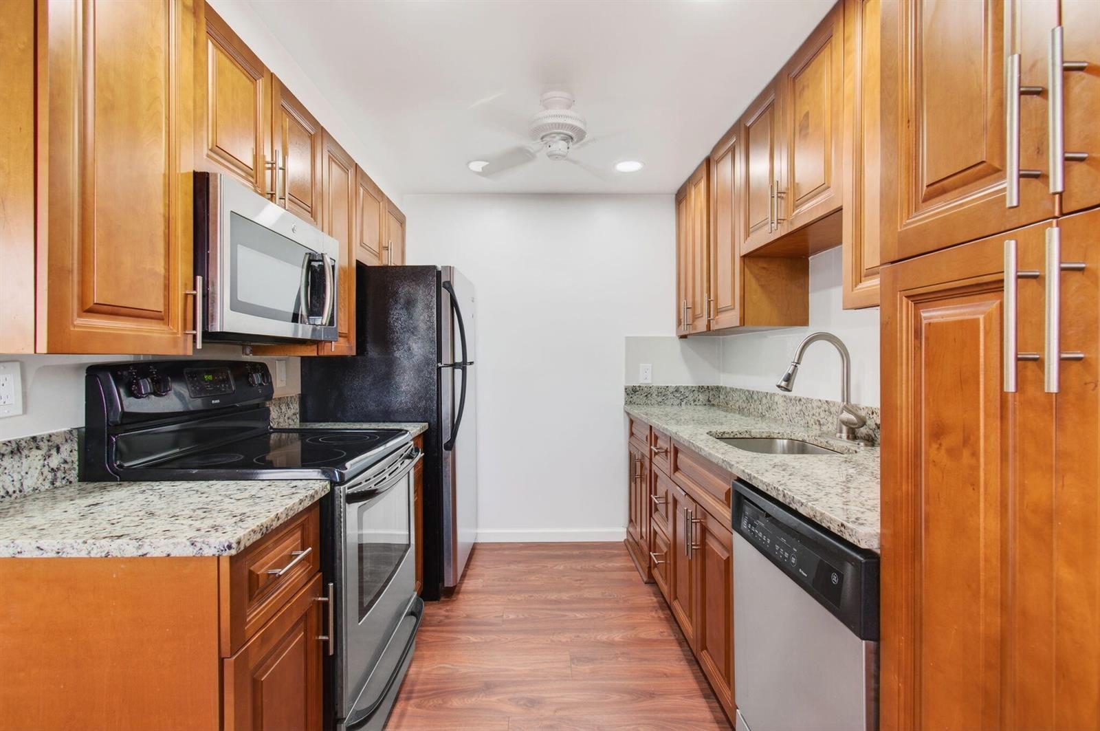 A galley kitchen features wood cabinets, granite countertops, and stainless steel appliances — 2035 Cornwall B, Boca Raton FL 33434, BOCA RATON, FL