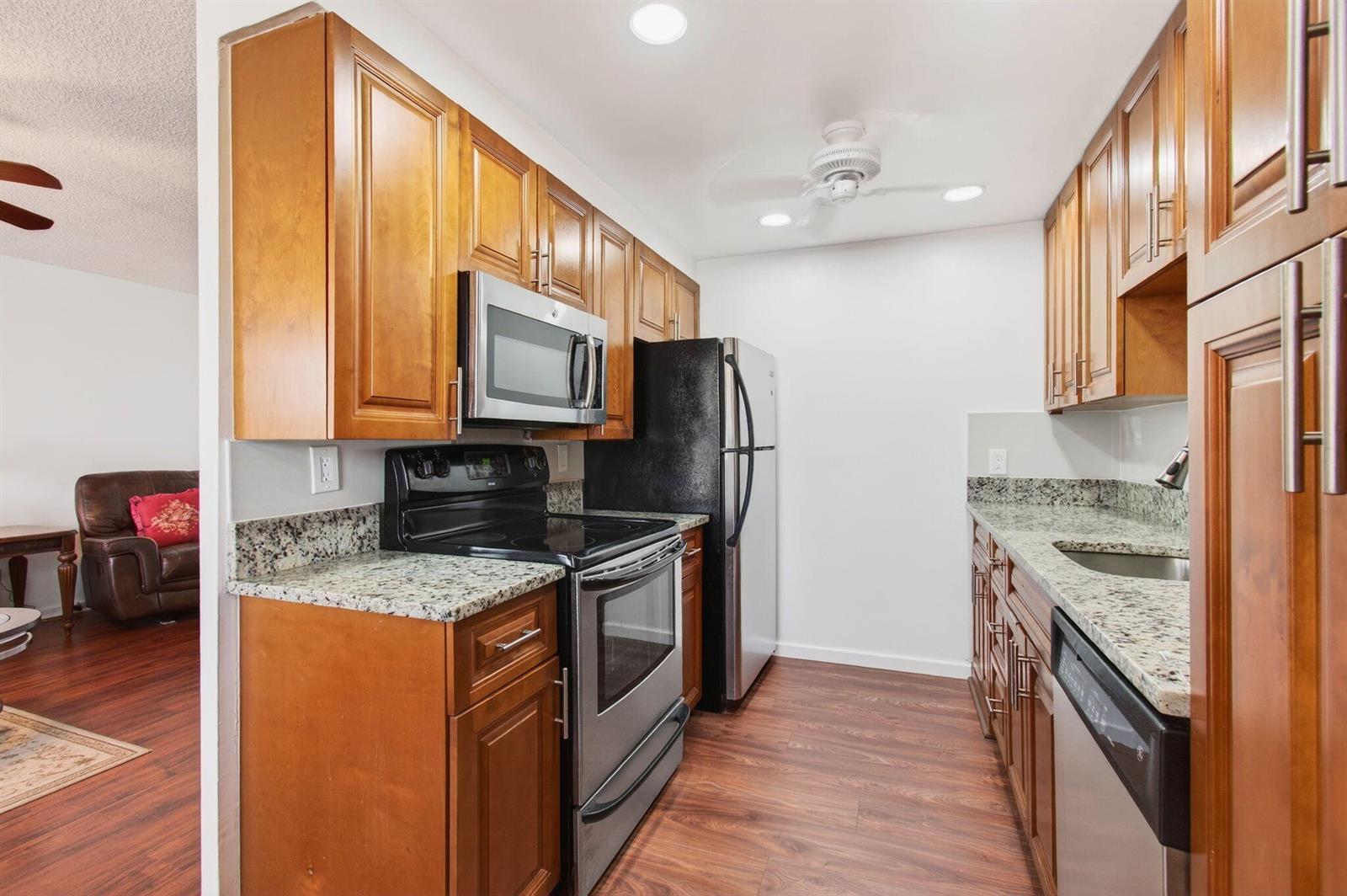 A galley kitchen features wood cabinets, granite countertops, and stainless steel appliances — 2035 Cornwall B, Boca Raton FL 33434, BOCA RATON, FL