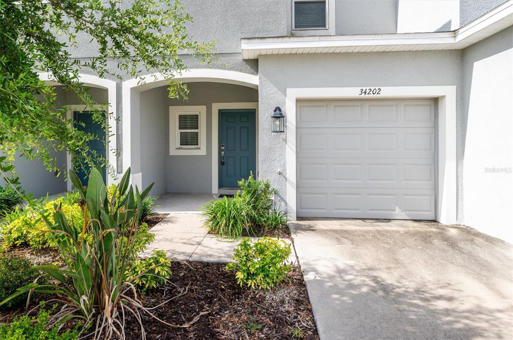 A gray townhouse exterior features a blue front door, a garage, and a small garden — 34202 POLACCA LANE, WESLEY CHAPEL, FL