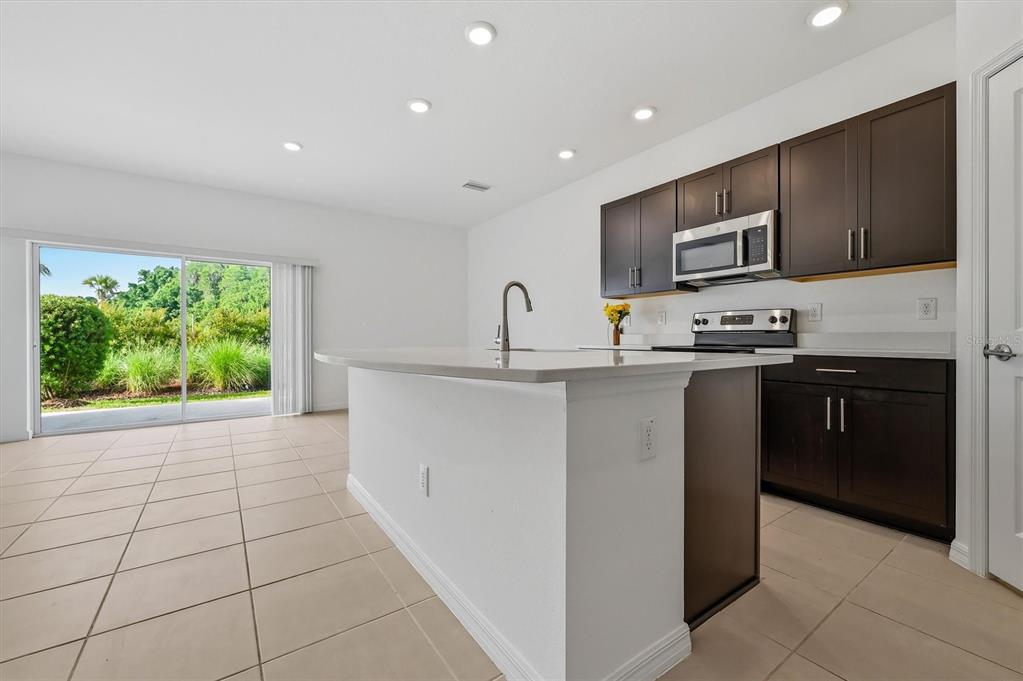 A kitchen with dark cabinets, a white island, and a sliding glass door to outside — 34202 POLACCA LANE, WESLEY CHAPEL, FL