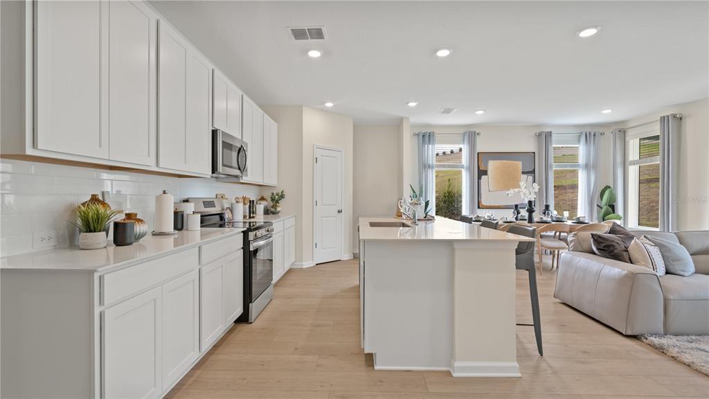 A modern kitchen with white cabinets, quartz countertops, and an island opens to a living area — 3121 ROCKWOOD WAY, MINNEOLA, FL