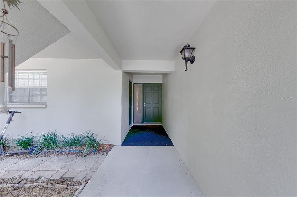 A covered entryway features a green front door, a wall-mounted lantern, and a concrete walkway — 68 COUNTRY CLUB DRIVE, LARGO, FL
