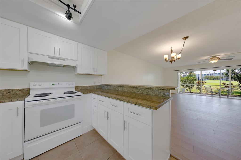 A kitchen with white cabinets and granite countertops overlooks a living area with sliding doors — 68 COUNTRY CLUB DRIVE, LARGO, FL