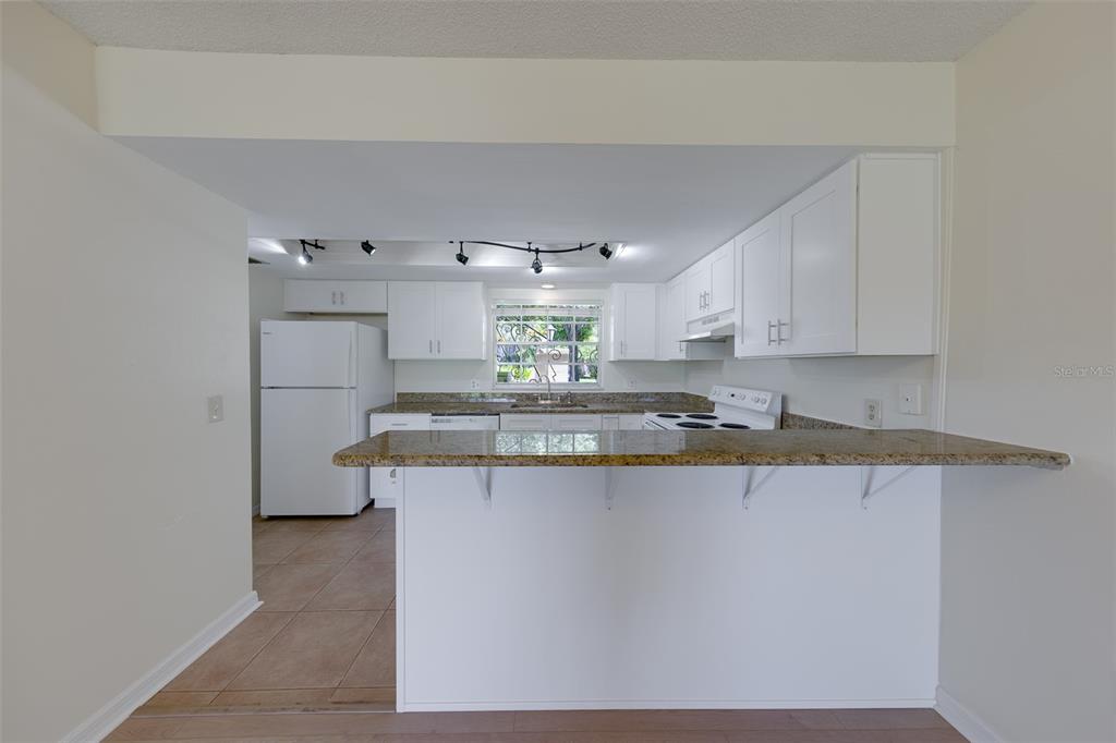 A kitchen features white cabinets, granite countertops, a breakfast bar, and white appliances — 68 COUNTRY CLUB DRIVE, LARGO, FL