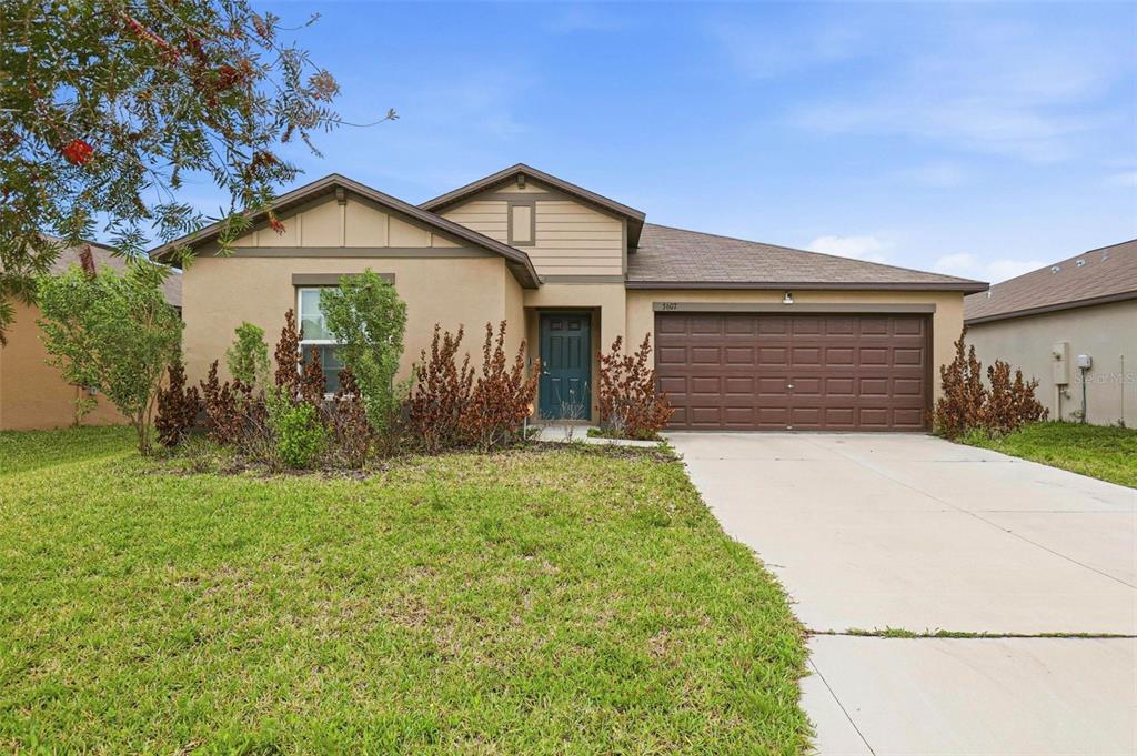 A single-story suburban house features a tan stucco exterior, a brown garage door, and landscaping — 3607 NATURAL TRACE STREET, PLANT CITY, FL