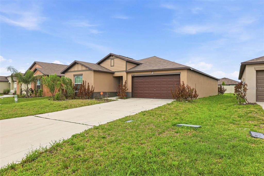 A single-story suburban house with a tan stucco exterior and a brown two-car garage — 3607 NATURAL TRACE STREET, PLANT CITY, FL