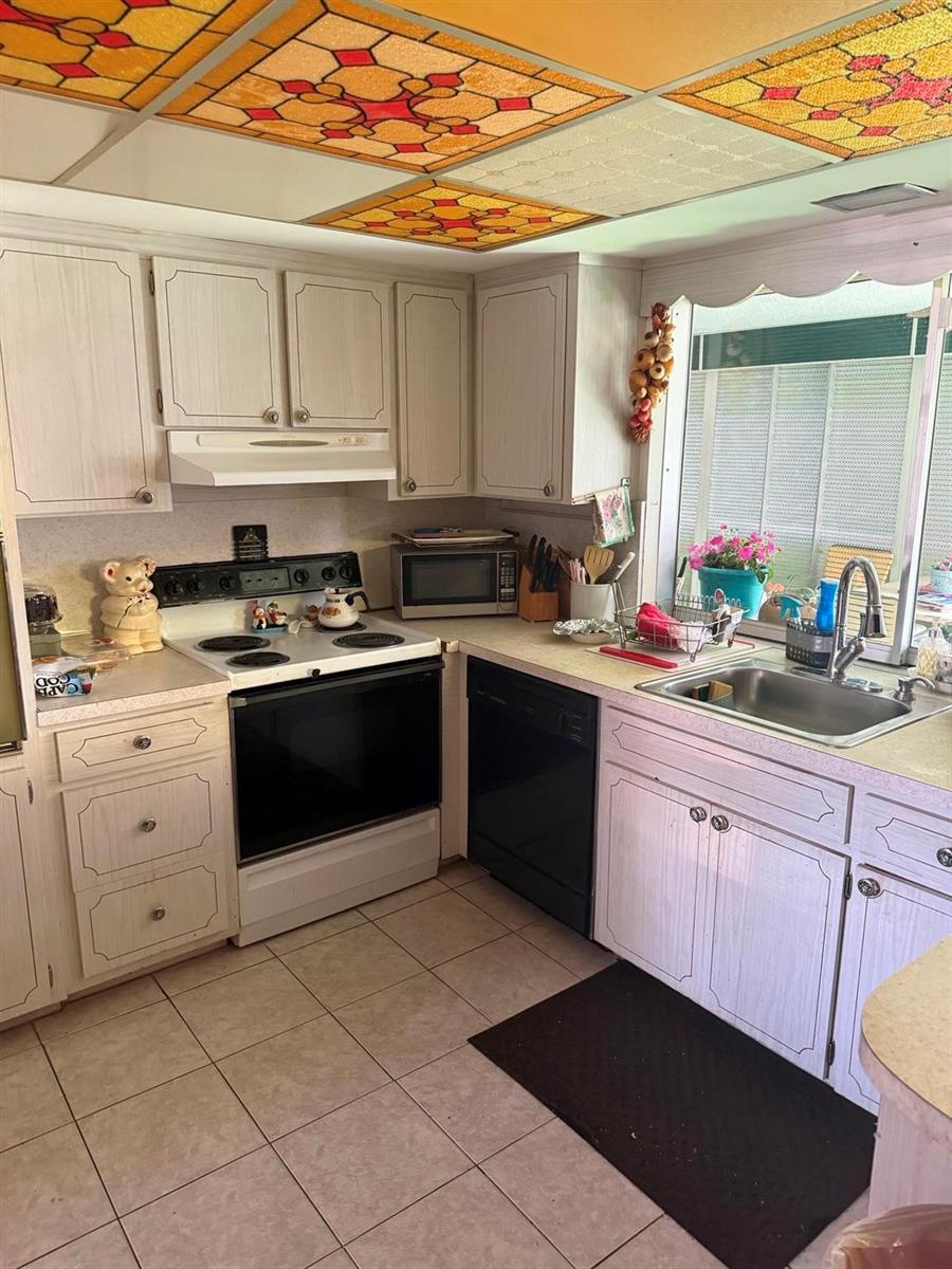 A kitchen features white cabinets, a black dishwasher, a white stove, and stained-glass ceiling panels — 626 S Crescent Drive, Hollywood FL 33021, HOLLYWOOD, FL