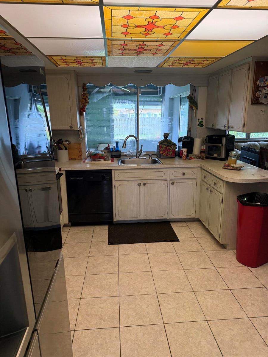 A kitchen features white cabinets, a black dishwasher, a stainless sink, and stained-glass ceiling panels — 626 S Crescent Drive, Hollywood FL 33021, HOLLYWOOD, FL
