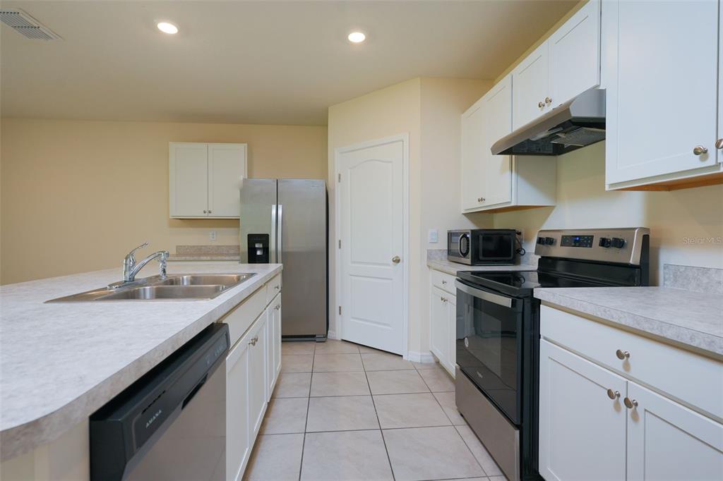A kitchen features white cabinets, stainless steel appliances, a center island, and tile flooring — 660 COTULLA DRIVE, KISSIMMEE, FL