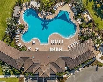 An aerial view shows a large, irregularly shaped swimming pool surrounded by lounge chairs and landscaping — 17220 HARVEST MOON WAY, BRADENTON, FL