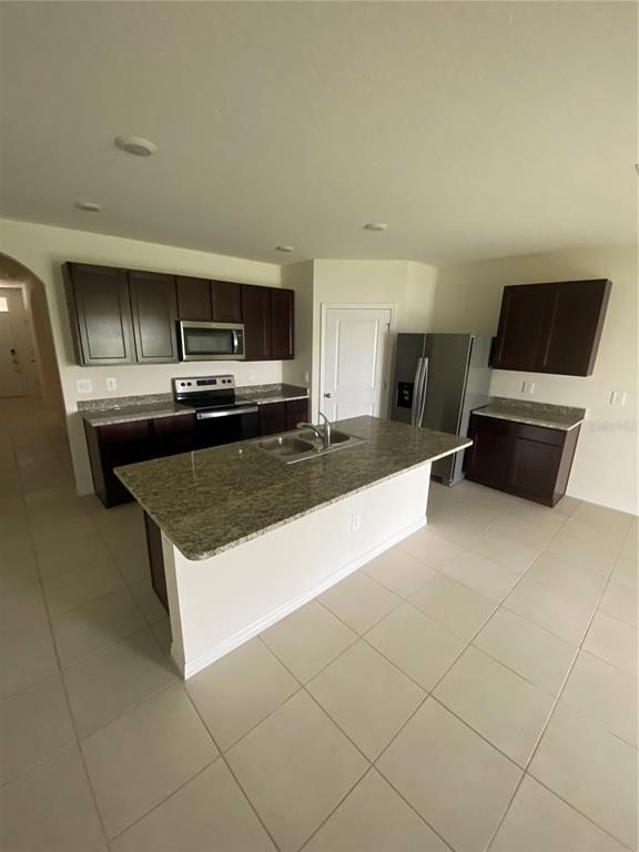 A kitchen features dark wood cabinets, granite countertops, a central island, and stainless steel appliances — 17220 HARVEST MOON WAY, BRADENTON, FL