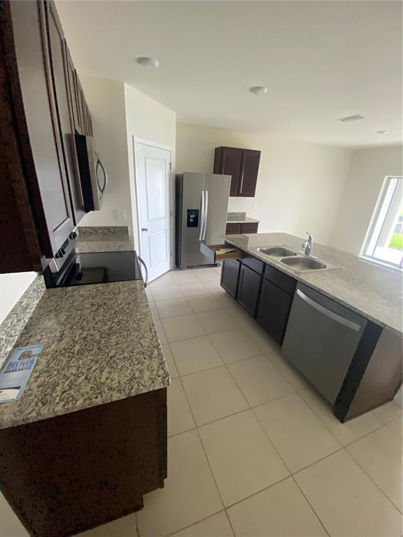 A kitchen features dark wood cabinets, granite countertops, stainless steel appliances, and tile flooring — 17220 HARVEST MOON WAY, BRADENTON, FL