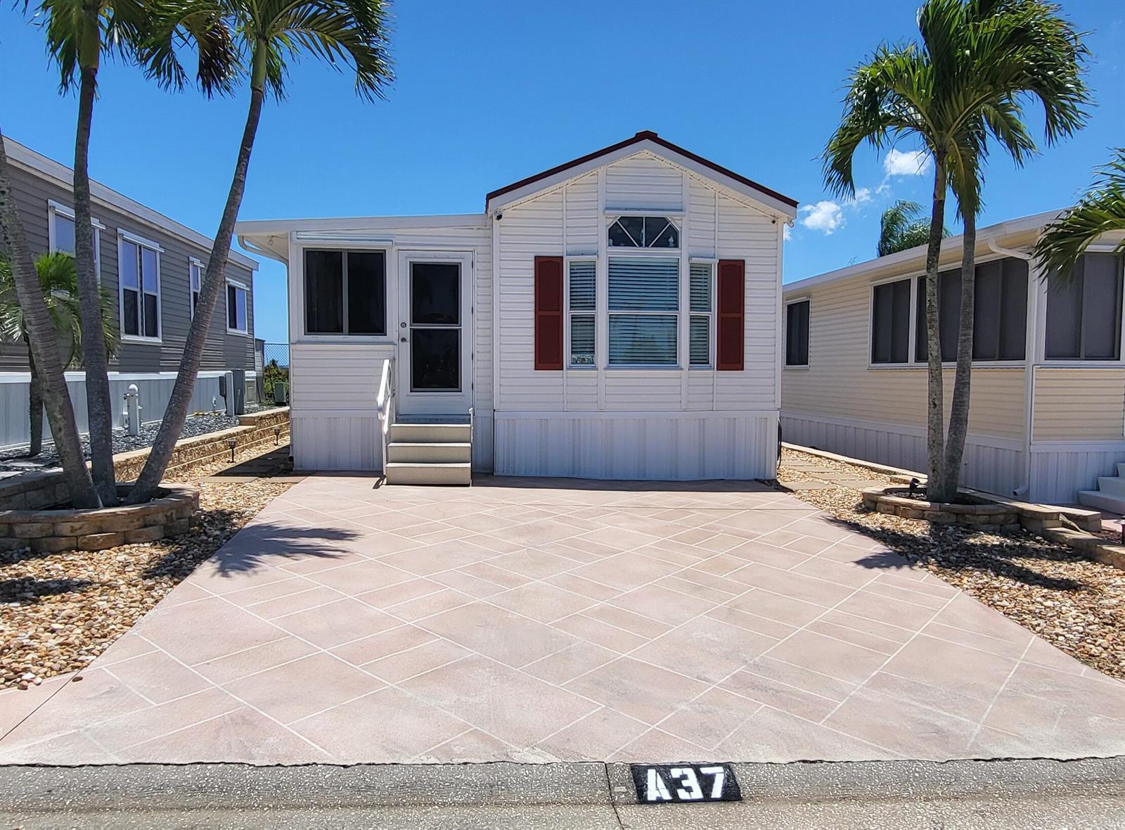 A white manufactured home with red shutters and a patterned concrete driveway under palm trees — 900 Juno Ocean Walk # 37, Juno Beach FL 33408, JUNO BEACH, FL