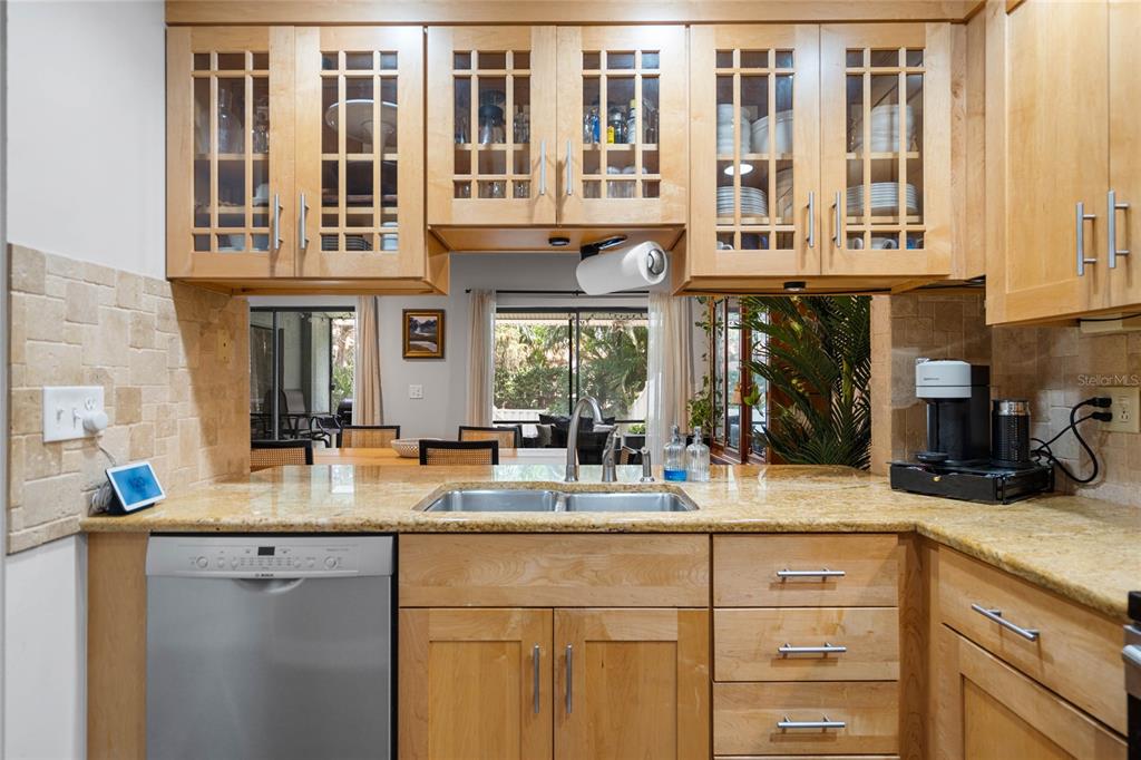 A kitchen features light wood cabinets, granite countertops, a stainless steel dishwasher, and a sink — 1092 SANABEL COURT NE, ST PETERSBURG, FL