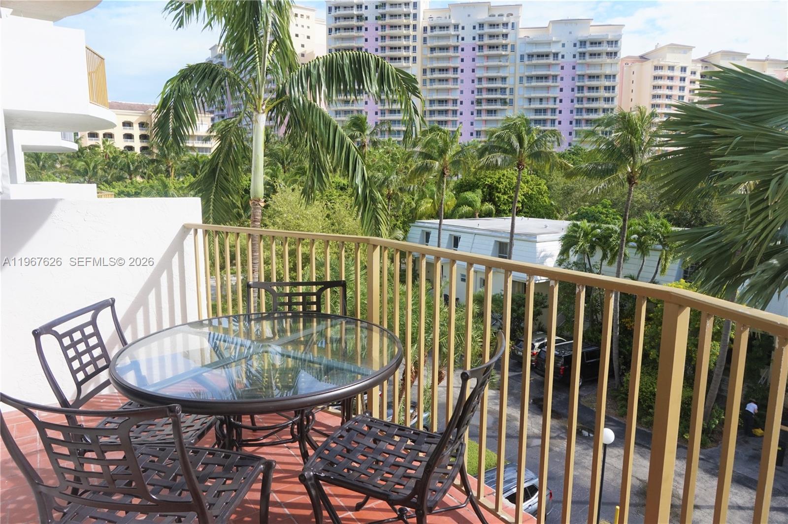 A balcony with a glass-topped table and chairs overlooks palm trees and apartment buildings — 210 Sea View Dr # 408, Key Biscayne FL 33149, KEY BISCAYNE, FL