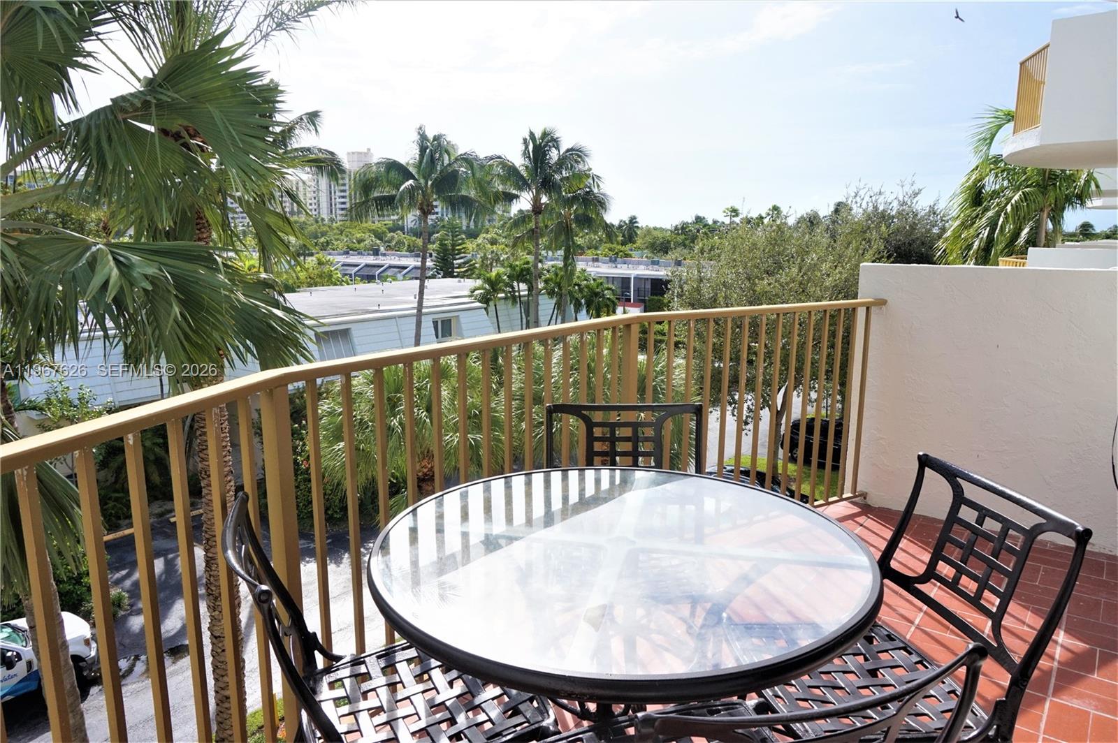A balcony features a glass-topped table, metal chairs, and a view of palm trees — 210 Sea View Dr # 408, Key Biscayne FL 33149, KEY BISCAYNE, FL