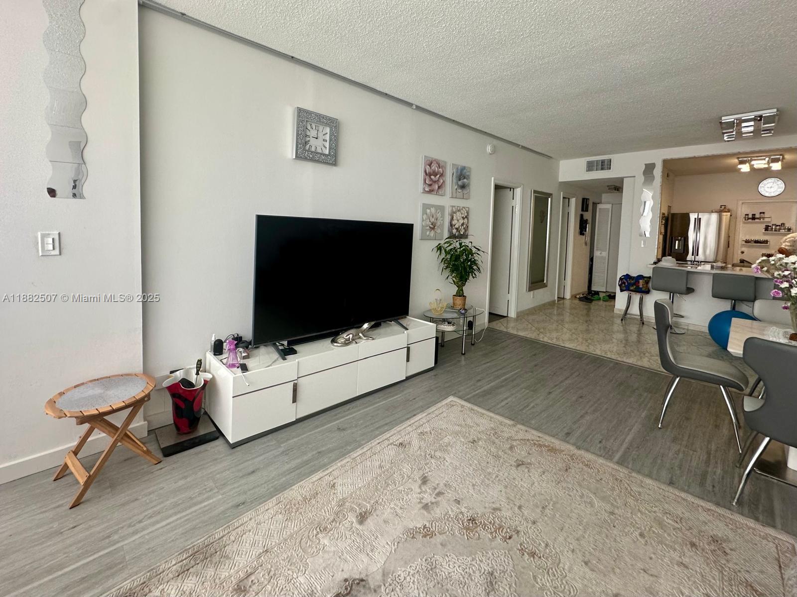 A living room features a television on a white console, gray flooring, and an area rug — 1825 S Ocean Dr # 6, Hallandale Beach FL 33009, HALLANDALE BEACH, FL