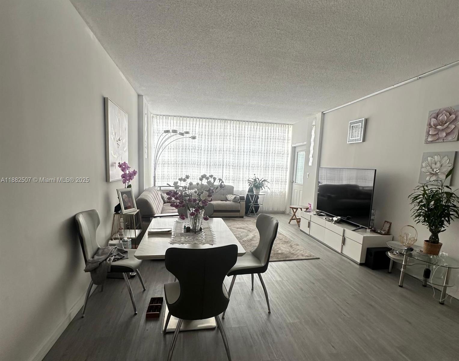 A living and dining area features light wood-look flooring, white walls, and floor-to-ceiling curtains — 1825 S Ocean Dr # 6, Hallandale Beach FL 33009, HALLANDALE BEACH, FL