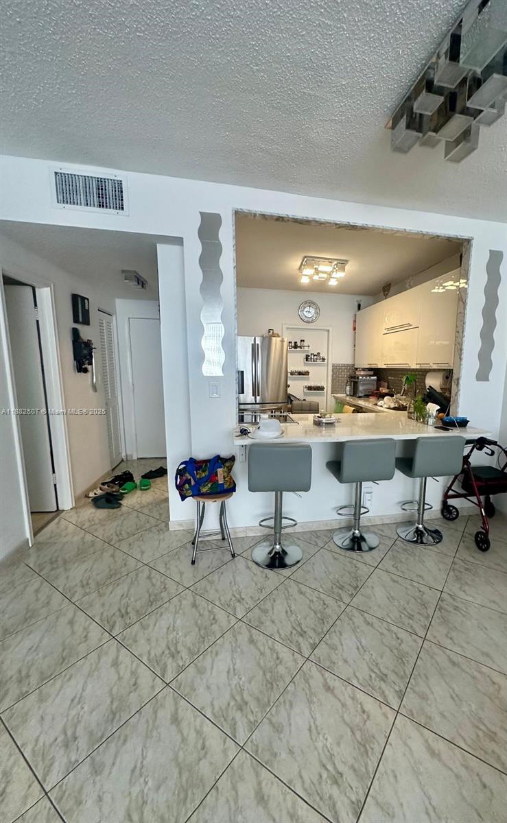 A kitchen with white cabinets and a breakfast bar opens into a tiled living area — 1825 S Ocean Dr # 6, Hallandale Beach FL 33009, HALLANDALE BEACH, FL