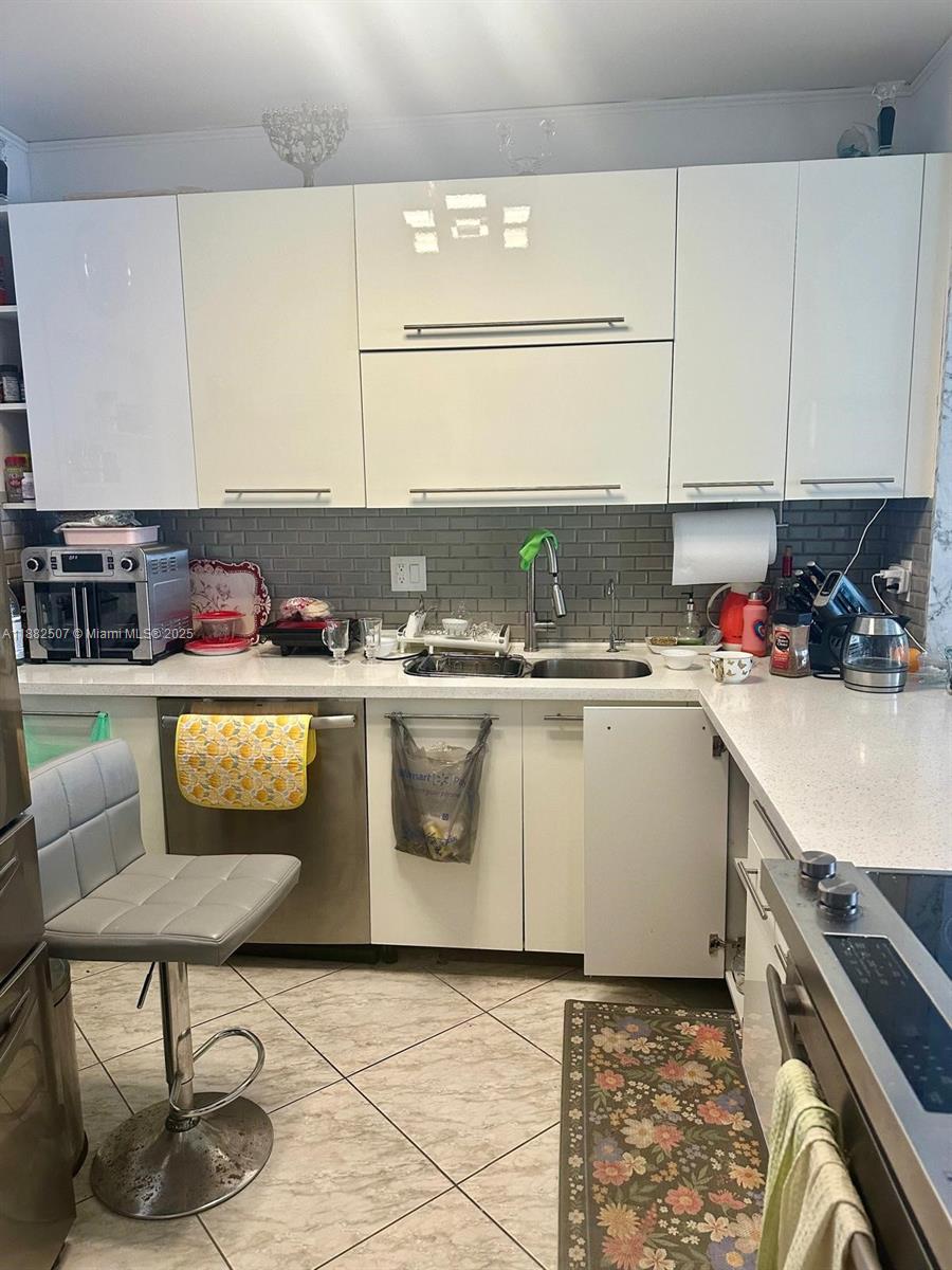 A kitchen features white cabinets, a gray subway tile backsplash, and stainless steel appliances — 1825 S Ocean Dr # 6, Hallandale Beach FL 33009, HALLANDALE BEACH, FL