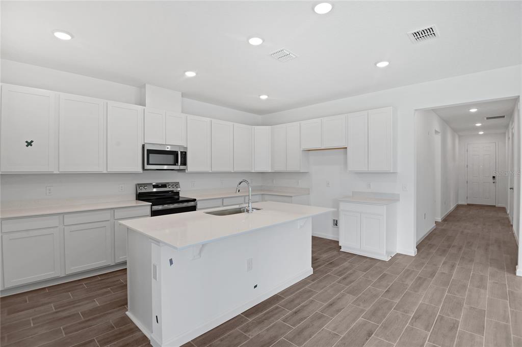 A modern kitchen features white cabinets, a central island, stainless steel appliances, and wood-look tile flooring — 5163 KINSLEY DRIVE, WINTER HAVEN, FL