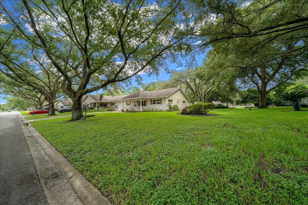 A single-story house with a light-colored exterior sits behind a large lawn and mature trees — 8720 SW 97TH STREET UNIT F, OCALA, FL