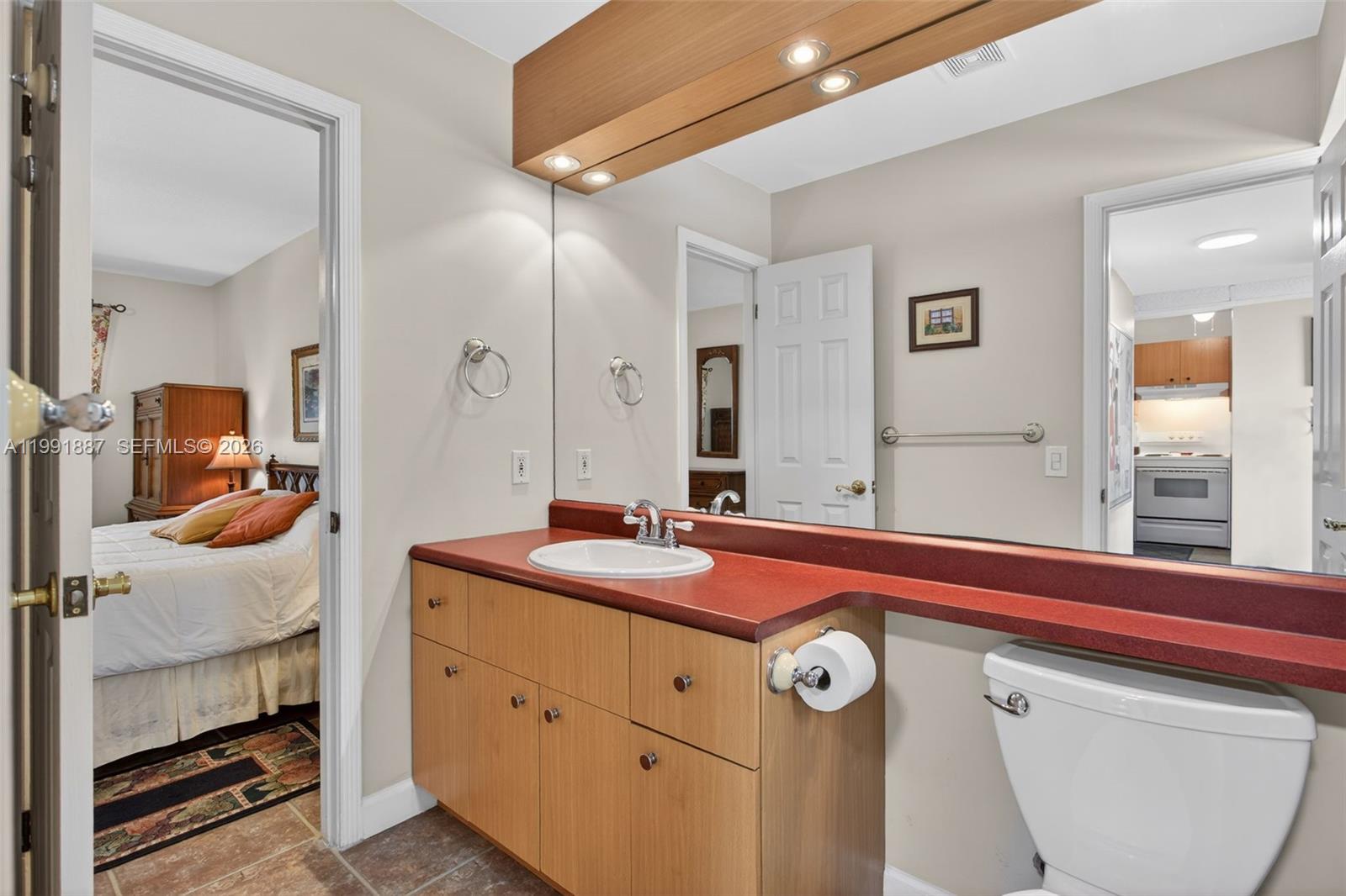 A bathroom with a red countertop, light wood vanity, and a large wall mirror — 4299 NW 16th St # 310, Lauderhill FL 33313, LAUDERHILL, FL