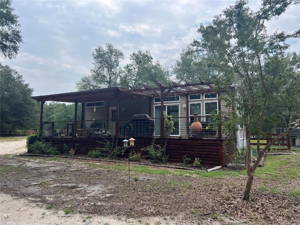 A single-story house with a large wooden deck and a pergola under mature trees — 3369 NE 53RD TERRACE, HIGH SPRINGS, FL