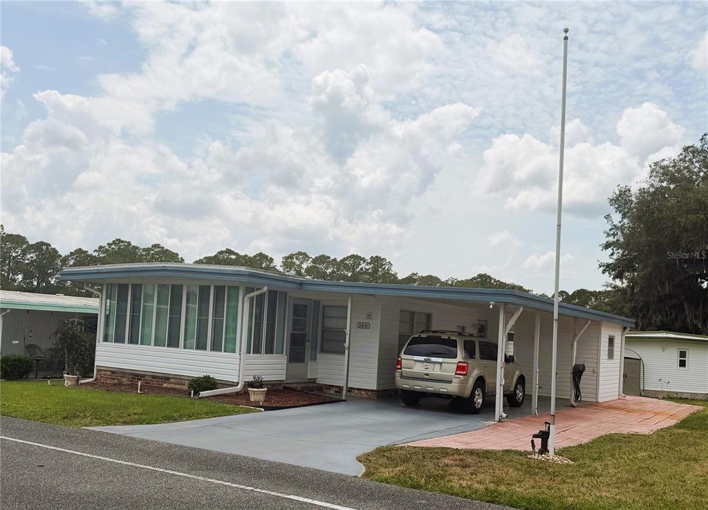A single-story manufactured home with a carport, a glass-enclosed porch, and a driveway — 340 PALO VERDE DRIVE, LEESBURG, FL