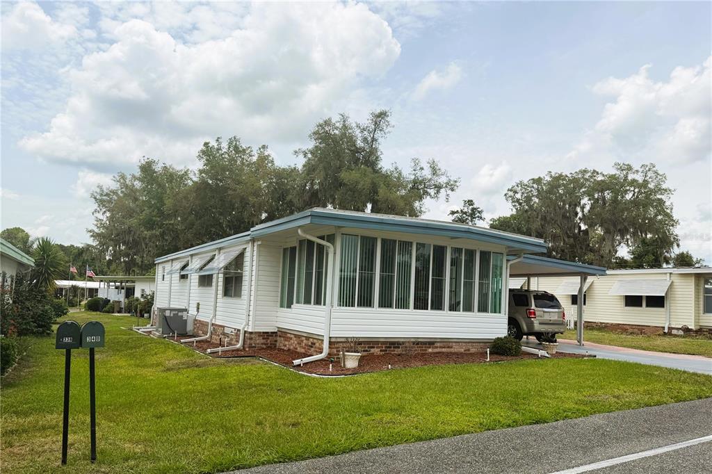 A white mobile home with a glass-enclosed sunroom and a carport sits on a lawn — 340 PALO VERDE DRIVE, LEESBURG, FL