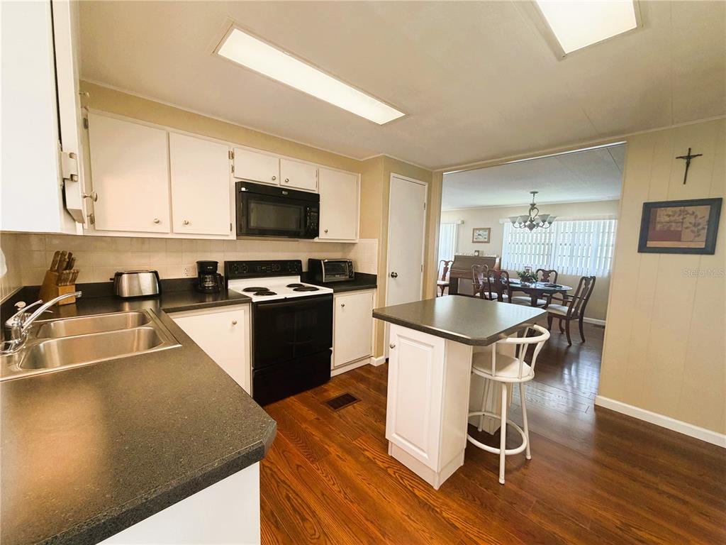 A kitchen with white cabinets, dark countertops, and a small island opens to a dining area — 340 PALO VERDE DRIVE, LEESBURG, FL
