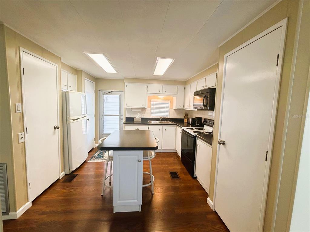 A kitchen features white cabinets, a central island, dark countertops, and wood-look flooring — 340 PALO VERDE DRIVE, LEESBURG, FL