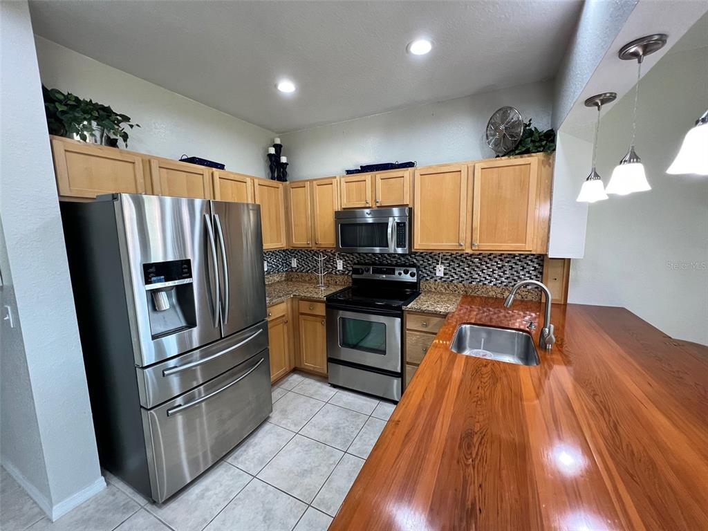 A kitchen features stainless steel appliances, light wood cabinets, and a polished wood countertop — 9570 SE 136TH PLACE, SUMMERFIELD, FL