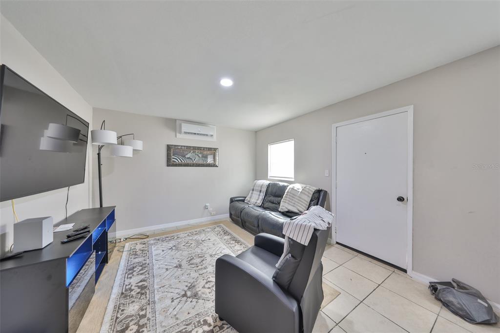 A living room features tile flooring, a black leather sofa, a recliner, and a wall-mounted television — 11708 BALM RIVERVIEW ROAD, RIVERVIEW, FL