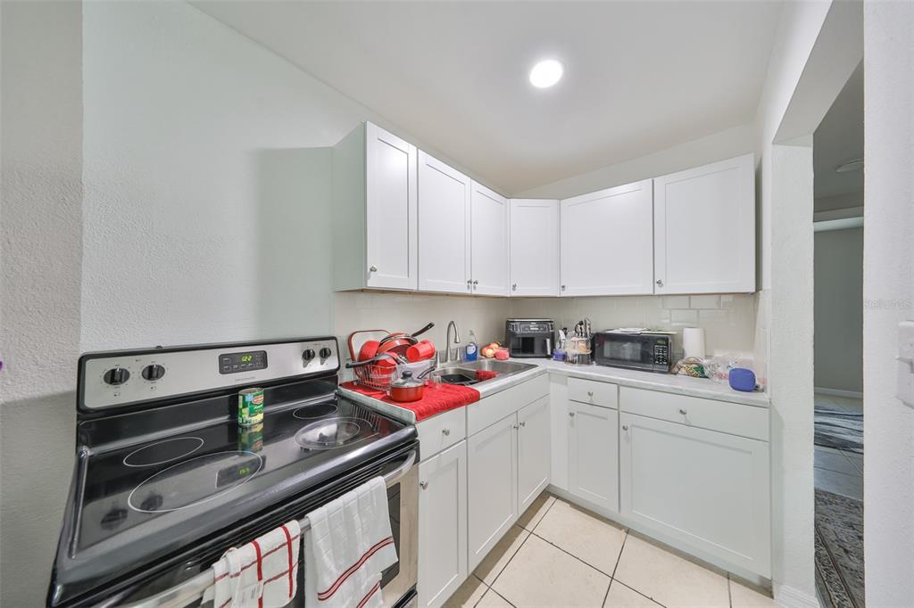 A small kitchen features white cabinets, a black electric stove, and light-colored tile flooring — 11708 BALM RIVERVIEW ROAD, RIVERVIEW, FL